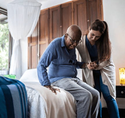 Caregiver assisting elderly man from bed
