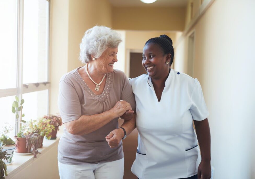 Happy elderly woman with caretaker in hallway