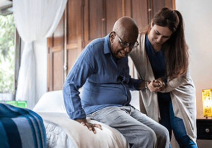 Caregiver assisting elderly man from bed